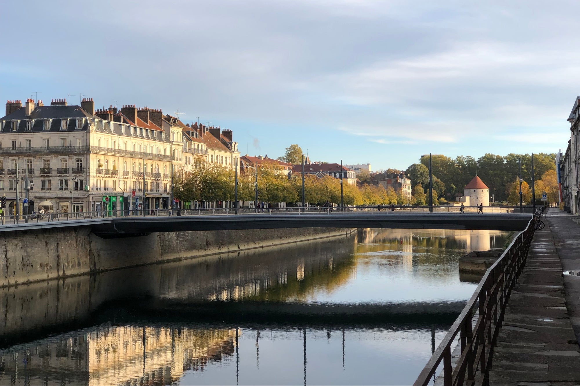 Reflection of the Besançon, France cityscape in water with a bridge and buildings.